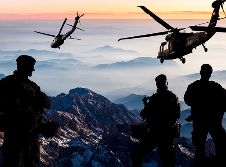 Military combat soldiers in the mountains with helicopters overhead. Exponent provides strategic military and warfighter support.
