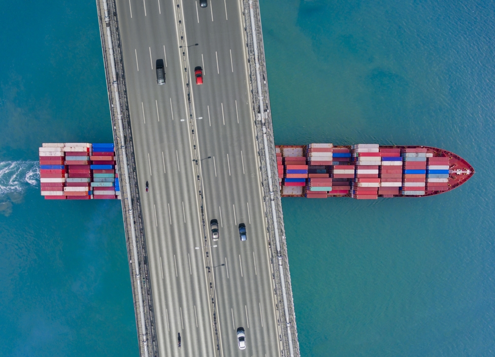 Aerial view of a cargo container ship passing under bridge.