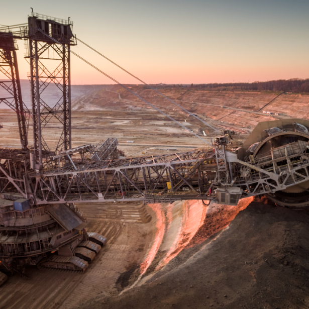 Crane-like machine excavating the earth, glowing red from sunlight, in the middle of a dirt plateau