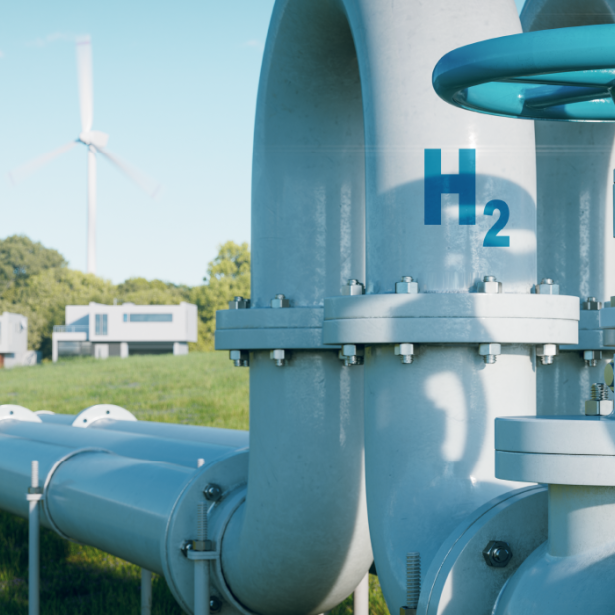 Hydrogen pipeline in a grassy field with wind turbines and buildings in the background