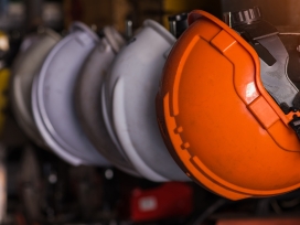 A row of orange industrial hard hats in a row. Exponent provides occupational and industrial workplace safety assessments