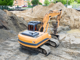 A construction excavator removes contaminated soil from a development site. Exponent helps with environmental site remediation.