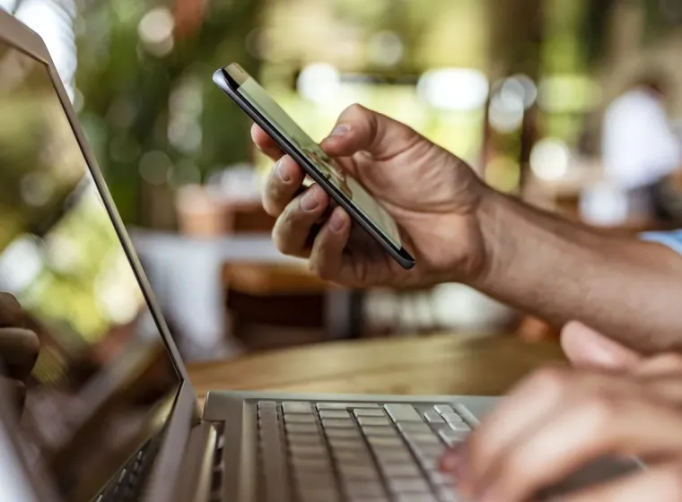 Man holds phone and uses laptop. 