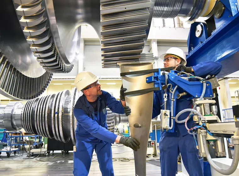 Two workers evaluate equipment on factory floor. Exponent conducts risk and safety analysis of mechanical engines.