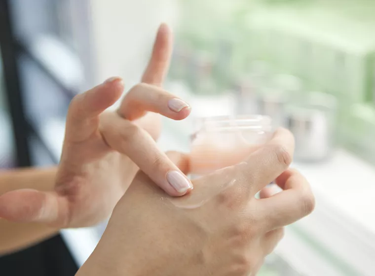 Person applies skin cream to hands. Exponent helps improve the chemical products and processes of cosmetics manufacturing.