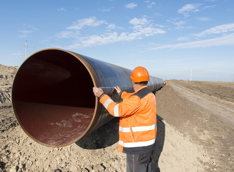 A person inspects a large oil pipeline before installation. Exponent materials engineers help improve the safety & performance of pipelines. 