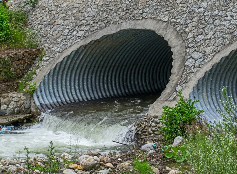 Water drains through pipes, under a bridge.