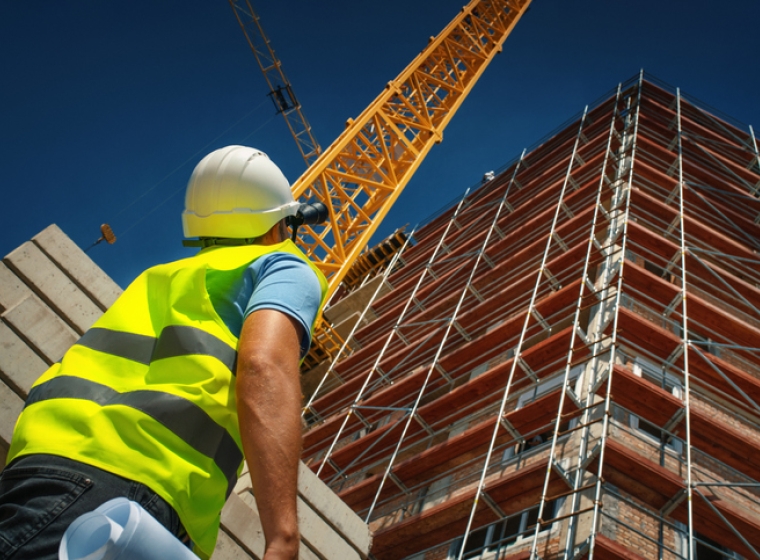 A construction worker looks up at a highrise building project. Exponent is the leader in construction engineering consulting.