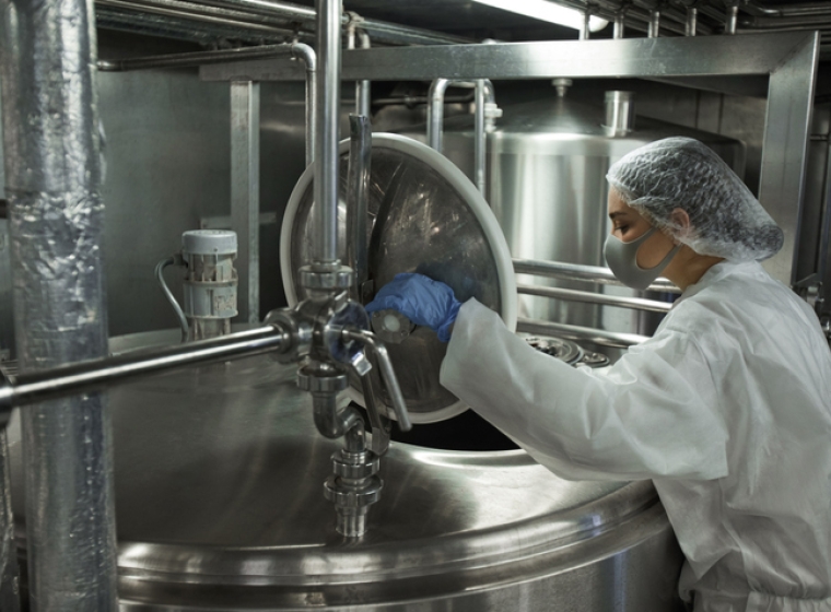 An industrial food factory worker opens a stainless steel vat. Exponent helps food and beverage manufacturers improve food safety.
