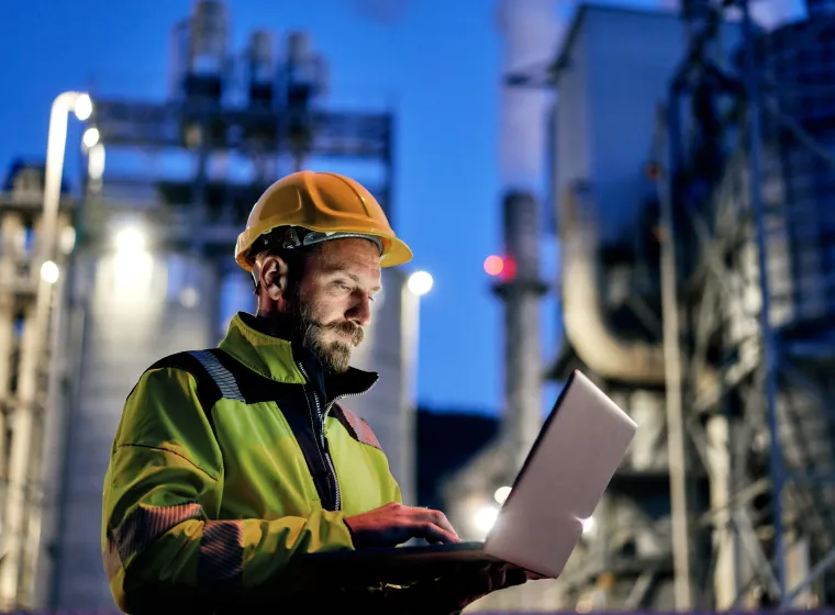 Young engineer wearing a helmet and using a laptop during his night shift. Engineering concept.