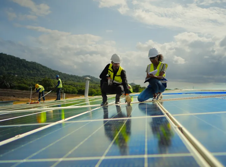 Team contractor, male engineer and female technicians wearing safety uniform, talking about installing plan, check the working system and maintenance solar panel of solar power plant to produce electricity on the roof of factory building. Industrial of renewable energy. Power generation from solar energy.