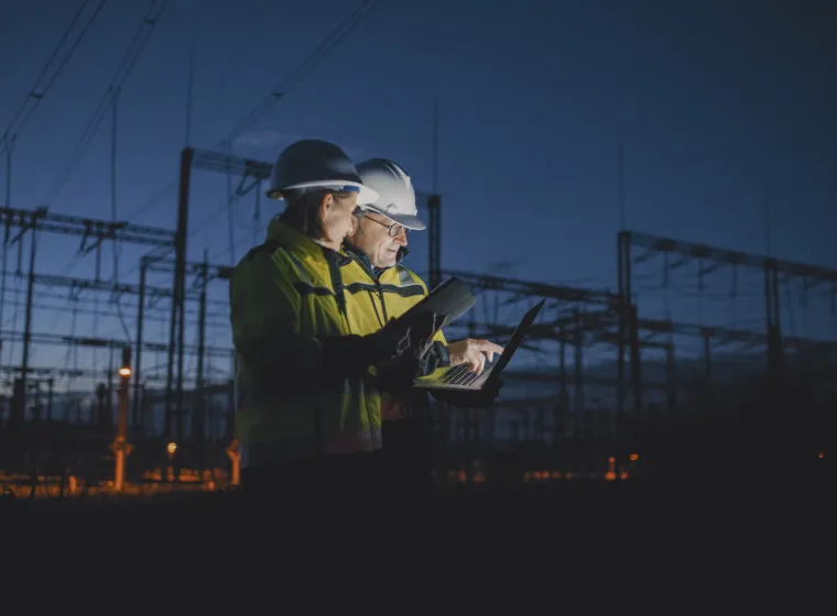 Electrical Engineers Discussing Over Laptop At Dark Power Plant During Night