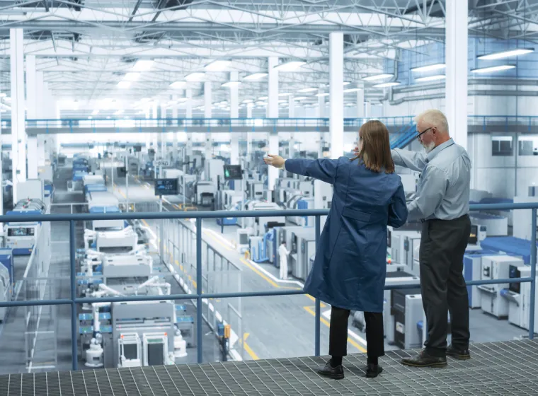 Experienced Male and Female Engineers Standing on a Platform with Their Back to Camera, Using Laptop Computer and Discussing Production at a Modern AI Automated Electronics Manufacture