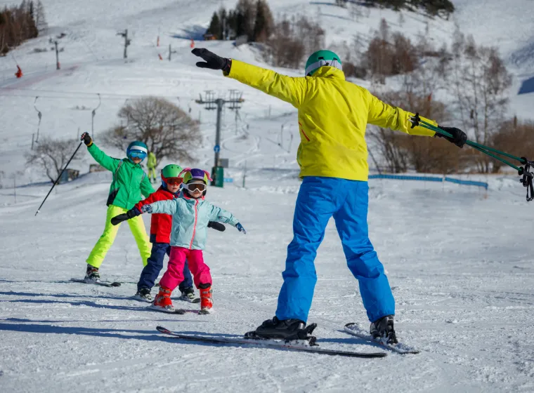 An instructor on a snowy mountain demonstrates skiing techniques to three children, all dressed in eye-catching winter gear on alpine resort