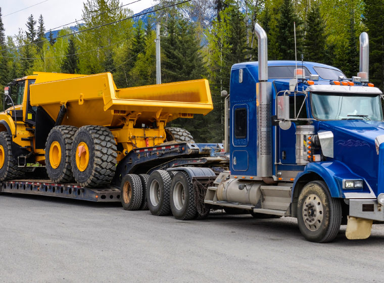 A flatbed semi-truck hauling a large commercial dump truck. Exponent helps innovate commercial transportation safety and performance.