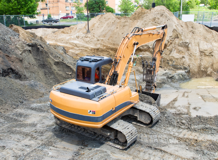 A construction excavator removes contaminated soil from a development site. Exponent helps with environmental site remediation.