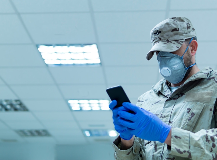 Soldier wearing mask using phone. Exponent's engineering expertise supports those within government sectors and private industry. 