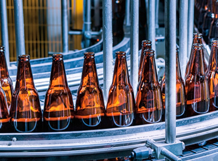 Dark glass bottles on a beverage manufacturing assembly line. Exponent helps clients improve food and beverage quality and safety.