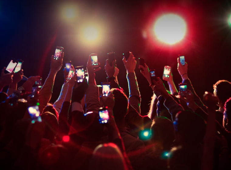 Crowd holds up cell phones at concert. Exponent provides technical engineering support for electronic device development.