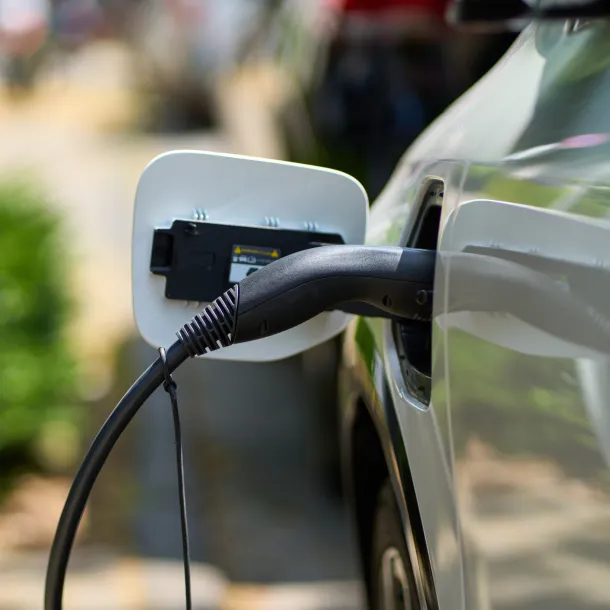 White e-car that is on the charging cable. The electric car is shown from the side where the environmentally conscious vehicle is being charged. 