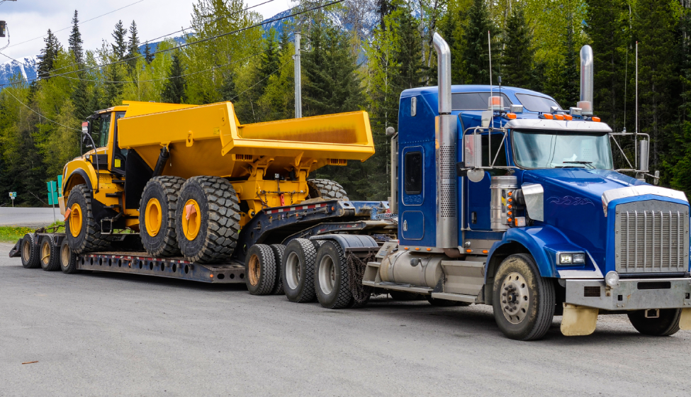 A flatbed semi-truck hauling a large commercial dump truck. Exponent helps innovate commercial transportation safety and performance.