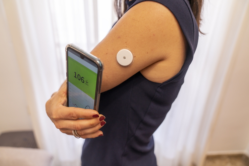 A person testing their glucose levels with a wearable device connected to a smartphone app