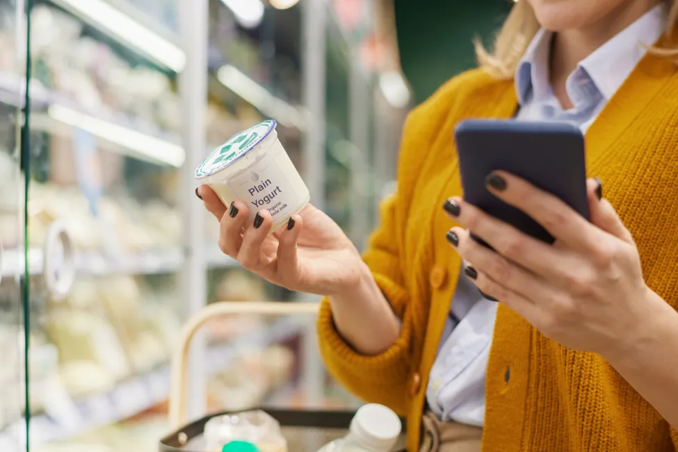 Close up of unrecognizable woman buying dairy products in supermarket and using smartphone, copy space
