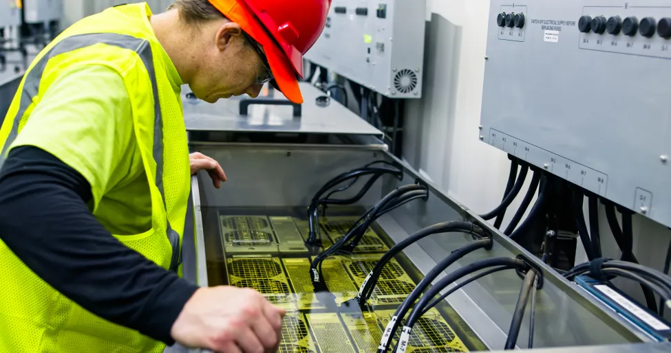 A technician working on an immersion cooling system in a data center for cryptocurrency mining, cloud services and AI computing in a large, temperature controlled warehouse in a remote location in Stutsman County, North Dakota. The server is submerged in a tank of a non-conductive fluid that draws away heat more efficiently than air, which lowers the energy and water consumption of the facility.