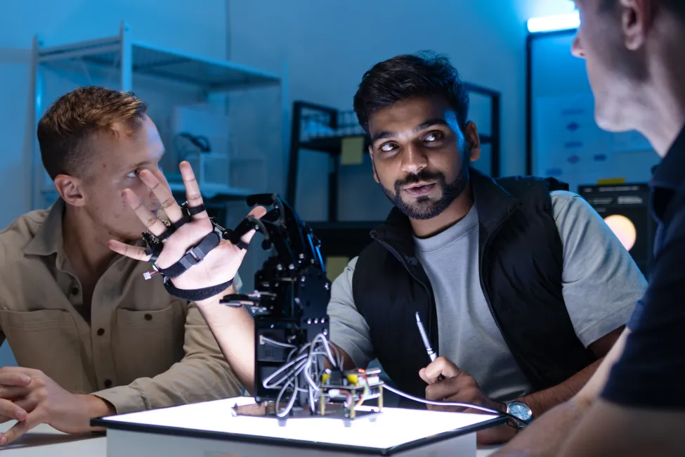 Engineers Working Together Around Robotic Hand Model During Future Technology Review and Artificial Intelligence Planning Discussion.
