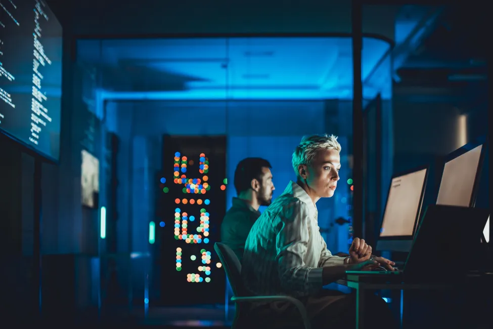 Short haired woman working at computer in modern data center with male colleague nearby