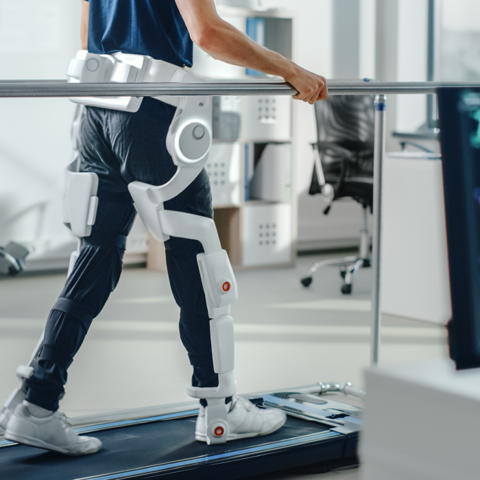 Person walking on treadmill with white electronic leg braces attaching a waist, with monitoring screen in the foreground showing vital signs