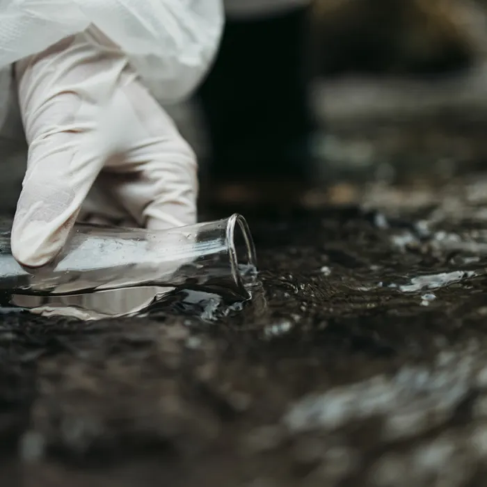 A person sampling fresh water using a test beaker in open environment. Evaluation exposure assessments and toxicity evaluations.