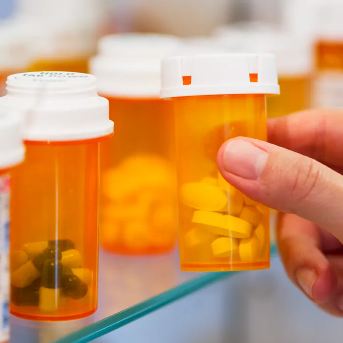 Hand picking up a bottle of prescription drugs off of a shelf