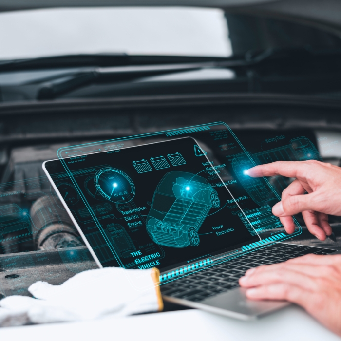 Mechanic working close to an automobile engine while using a laptop. A screen-based automotive diagnostic application.