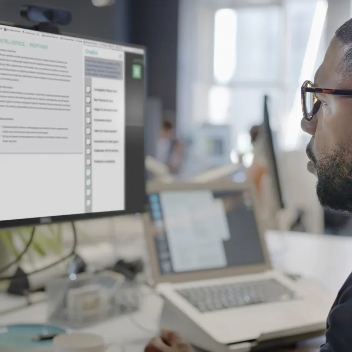 black man’s face looking into a computer screen in an open plan working office. Type is being added to the screen by an Artificial intelligence, AI, chatbot.