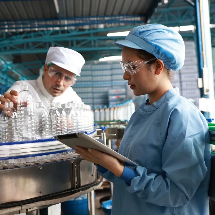 The lab technicians and hygienists with clean suits and PPE examining water bottles in bottling plant mineral water drinking water factory