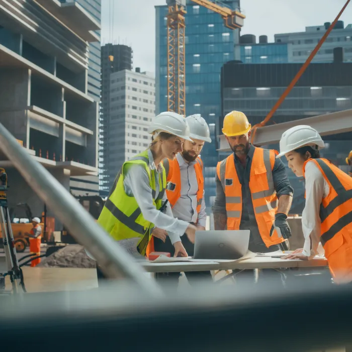 Female Civil Engineer Using a Laptop Computer and Talking with General Workers at a Residential Building Construction Area. Female and Male Employees Oversee the Real Estate Project Plan 