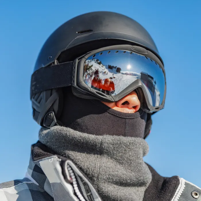 Close-up of an Asian man skiing in the European Alps. The skier is wearing protective gear, reflecting the clear blue sky and snow-covered mountains. The image captures the essence of winter sports and adventure.
