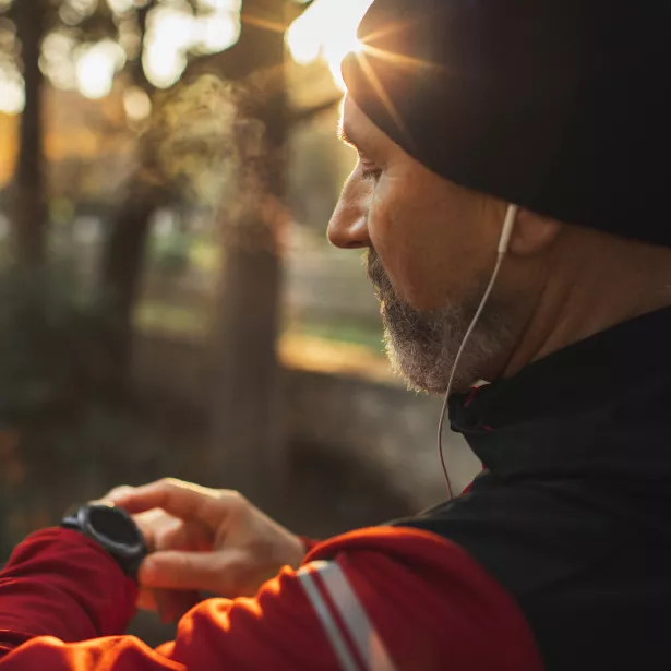 A man on checking his smart watch while on a run through a trail.