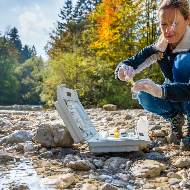 Mature female biologist adding reagent into a vial with water sample near river.