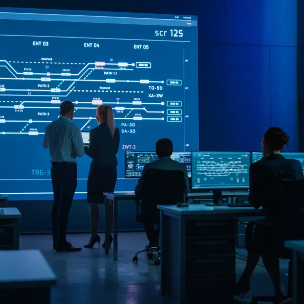 Telecommunications Company System Control and Monitoring Room with Diverse Multicultural Team of Professionals Working on Computers. Big Screen Display Showing Infrastructure Infographics. Back View