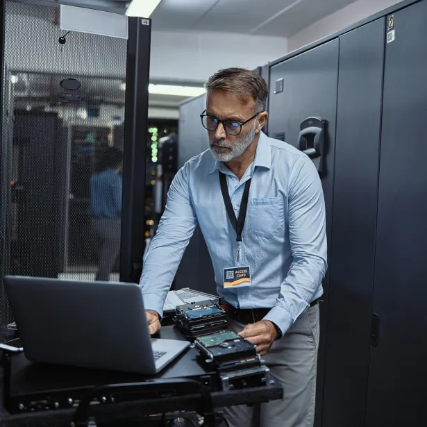Mature software engineer using a laptop in a server room. IT technician working on network programming with online technology. Protecting information on the internet with cyber security management