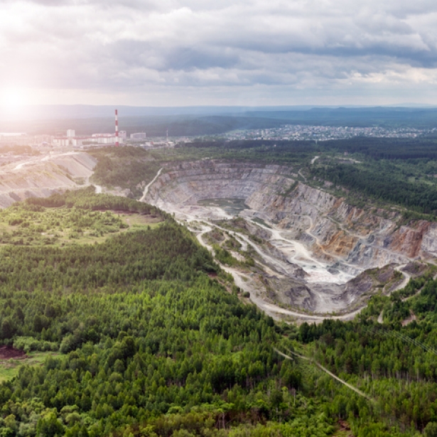 An aerial view of an open pit copper mine in a forested area. Exponent helps improve biodiversity and sustainability.