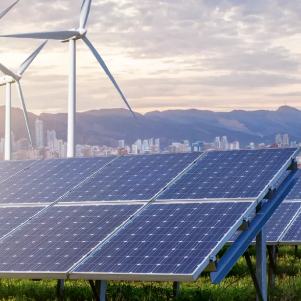 Solar panels and wind turbines against the backdrop of a city and mountains at sunset