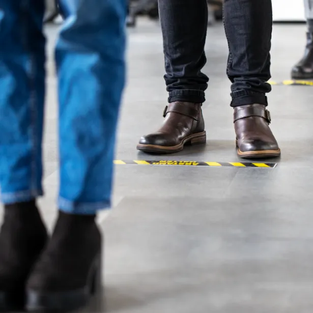 People standing on floor markers to social  distance while waiting in line 
