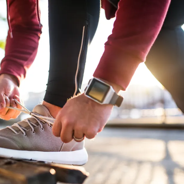 Close up of man in exercise clothing bending down to tie his shoe on a park bench