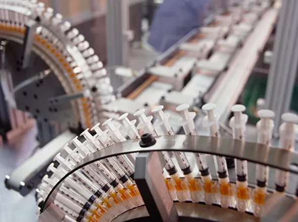 Two conveyor belts with hundreds of syringes merging into a third conveyor belt in a manufacturing plant