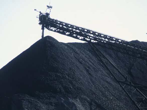Huge mounds of black coal with crane hovering over top of mound