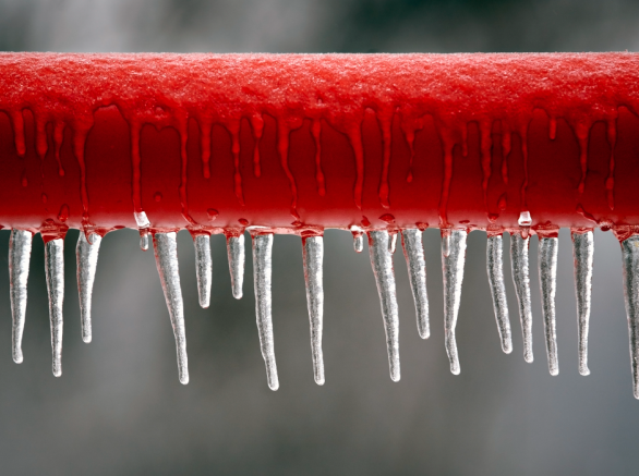 Close up of a horizontal red pipe that is frozen with icicles hanging from it 
