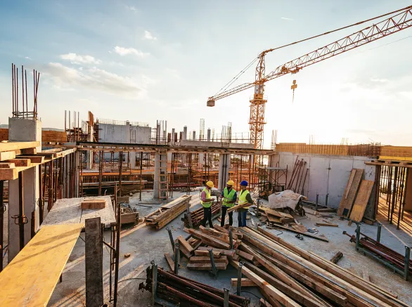 Construction industry concept - architects and engineers discussing work progress between concrete walls, scaffolds and cranes.